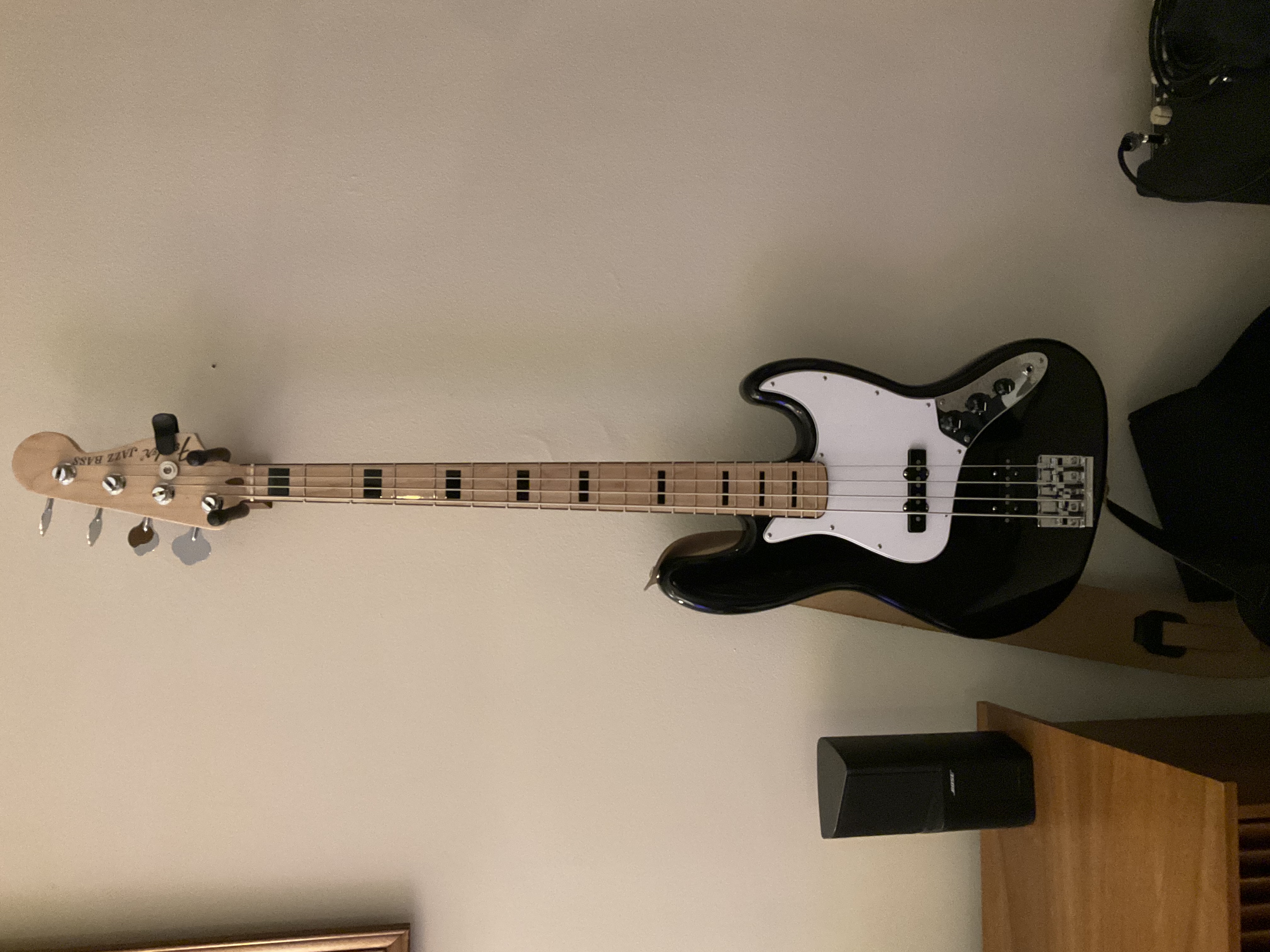 A black Fender jazz bass with a white pick guard and black block inlays on a maple neck