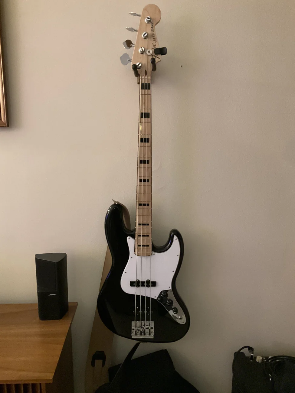 A black Fender jazz bass with a white pick guard and black block inlays on a maple neck